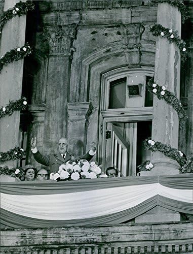 Гроздобер фотографија на Чарлс де Гол, кој ги гестивира рацете од балкон, сопругата Ивон на задниот дел.